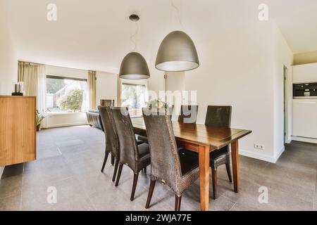 Una luminosa e spaziosa area da pranzo moderna con tavolo in legno, sedie in vimini e eleganti lampade a sospensione. Foto Stock