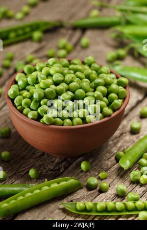 Piselli verdi biologici freschi in cialde chiuse e aperte, semi di piselli sparsi, piselli verdi sgusciati in una ciotola di argilla su uno sfondo di legno invecchiato. prote vegetale Foto Stock