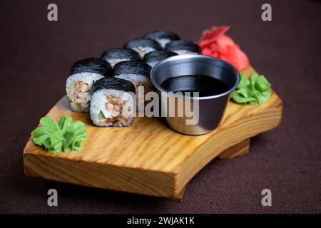 Assortimento di sushi con una varietà di panini e sashimi splendidamente disposti su un piatto di legno, accompagnati da bacchette e un lato di soia saporita Foto Stock