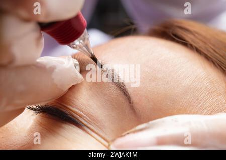 Il maestro di bellezza esegue il trucco permanente delle sopracciglia in un salone di bellezza, primo piano. Le mani di un cosmetologo che fa il microblading delle sopracciglia. Tatuaggio Foto Stock