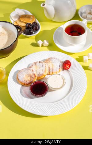 Deliziosa colazione con pancake al formaggio, farinata d'avena, tè, miele, marmellata frutta su tavola gialla Foto Stock