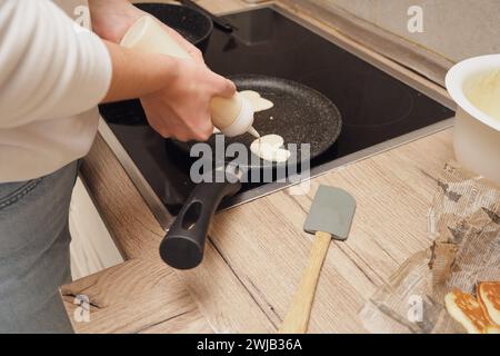Donna che versa il latte in una padella con pancake a forma di cuore Foto Stock