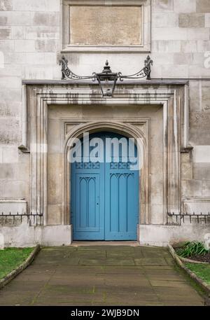 Londra, Regno Unito -​ dicembre 25, 2023 - porta medievale ad arco con una lanterna sopra di essa. Dettagli della porta della chiesa chiusa in legno blu in un muro di pietra gotica presso la città Foto Stock