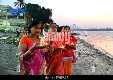 Donne indiane che eseguono un'offerta di preghiera serale con una lampada d'argilla galleggiante sulla riva del fiume Gange a Kolkata, India. Foto Stock