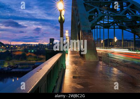 L'ora di punta mattutina sul Newcastle Tyne Bridge è stata utilizzata come una lunga esposizione in modo che le luci delle auto siano mostrate come sentieri leggeri. Il sole sta sorgendo sullo sfondo. Foto Stock