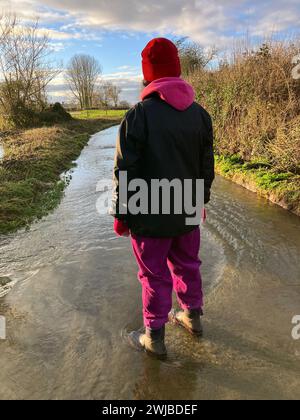 Donna da dietro, in piedi in acque alluvionali, nella Country Lane, Somerset, Inghilterra Foto Stock