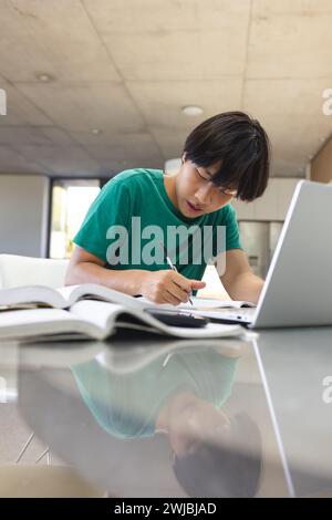 Adolescente ragazzo asiatico che studia intensamente a un tavolo Foto Stock