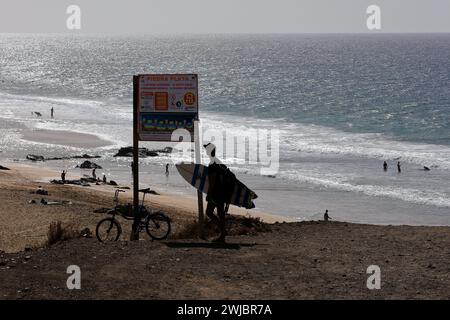 Surfista con tavola da surf in sagoma studia bacheca informativa presso la spiaggia di surf Piedra Playa, Fuerteventura scattata nel novembre 2023 Foto Stock