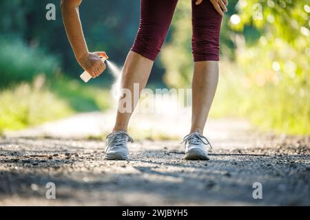 Donna che spruzza repellente per insetti contro le zanzare e spuntare la gamba prima di fare jogging in natura Foto Stock