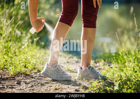 Donna che spruzza repellente per insetti contro le zanzare e spuntare la gamba prima di fare jogging in natura Foto Stock