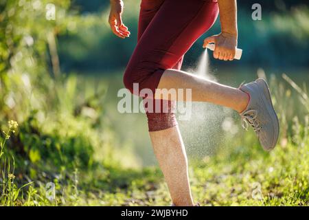 Donna che spruzza repellente per insetti contro le zanzare e spuntare la gamba prima di fare jogging in natura Foto Stock