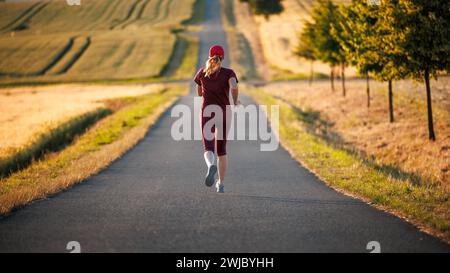 Corsa su strada. Donna che indossa un abbigliamento sportivo Bordeaux e corre all'aperto. Fitness, jogging e attività sportive Foto Stock