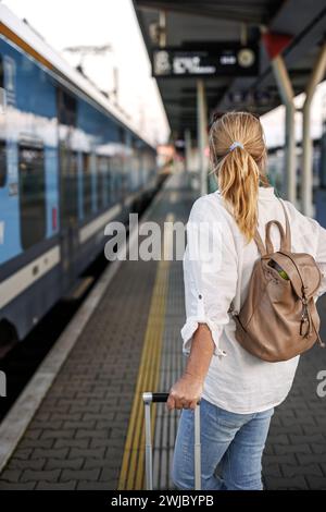 Donna che viaggia in treno. Turista con zaino e valigia in attesa di imbarcarsi sul treno al binario della stazione ferroviaria. Stile di vita da solo Foto Stock