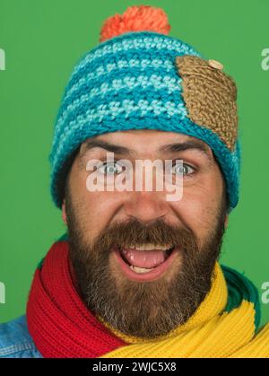Ritratto di un bell'uomo con barba in maglia di cappello e sciarpa. Uomo barbuto felice con sciarpa colorata e cappello di lana. Uomo alla moda in abbigliamento invernale Foto Stock