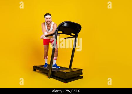 Ritratto a grandezza naturale dell'attrezzatura da tapis roulant da uomo sportivo, stanco e affascinante, spazio vuoto isolato su sfondo di colore giallo Foto Stock