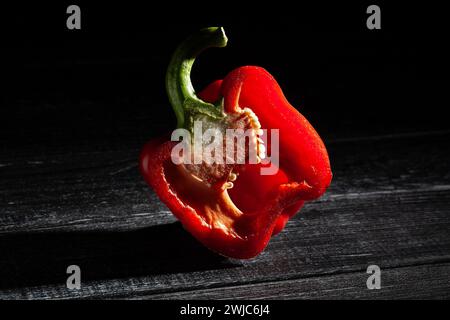 peperone rosso a fette su sfondo di legno nero Foto Stock