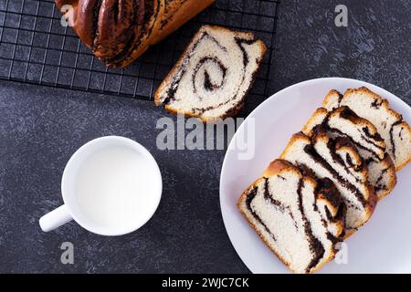 Pezzi di panino con semi di papavero su piatto bianco con tazza di latte su sfondo nero, vista dall'alto Foto Stock