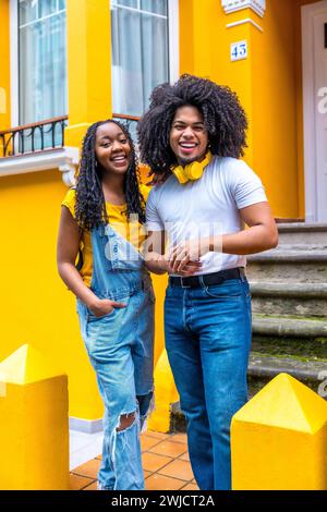 Ritratto verticale di una graziosa coppia africana accanto a una casa gialla Foto Stock