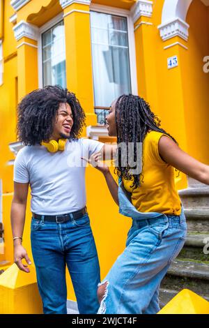 Felice coppia africana con cuffie rilassanti accanto a una casa con facciata gialla Foto Stock