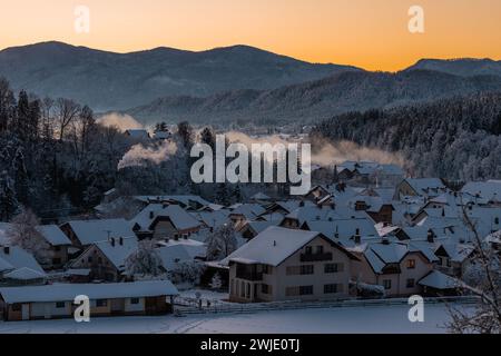 Dettaglio delle case ricoperte di neve nel bellissimo villaggio di Ljubno ob Savinji, casa di salto con gli sci femminile. La mattina presto, con il sole alle porte del ris Foto Stock