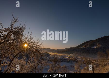 Splendido villaggio di Ljubno ob Savinji, sede di gare femminili di salto con gli sci. Panorama invernale dall'alto del villaggio la mattina presto. Il sole sorge sopra Foto Stock