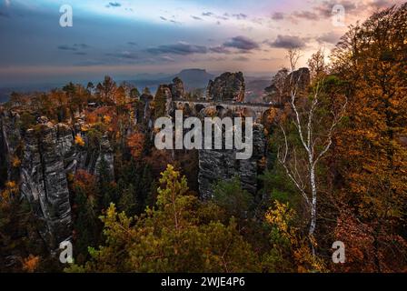 Sassonia, Germania - il ponte Bastei con un sole alba autunnale con fogliame colorato e cielo. Bastei è famosa per la splendida formazione rocciosa di Sax Foto Stock