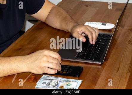 Giovane adulto in abiti neri con volto nascosto. Il truffatore malintenzionato utilizza dispositivi mobili. Il truffatore chiama. Racchetta mobile. L'hacker dirotta per telefono. Frode sul conto del cellulare. Truffa. Foto di alta qualità Foto Stock