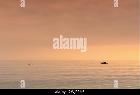 Una piccola barca a nachor in un oceano calmo al tramonto Foto Stock