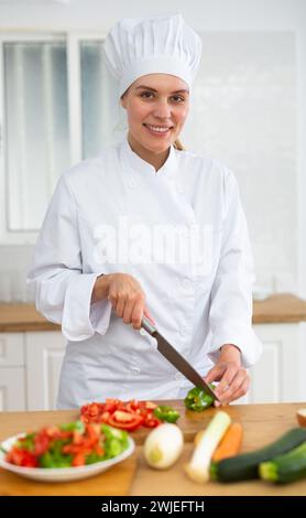 Donna proffesional cuoca in bianco uniforme tagliando verdure Foto Stock