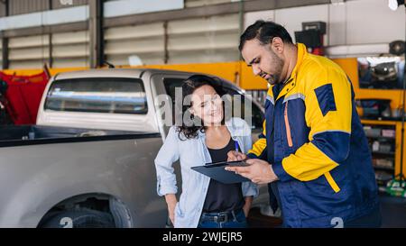 Le donne del cliente sono contente dell'elenco di controllo dell'assistenza auto dei lavoratori meccanici nell'officina del centro auto Foto Stock