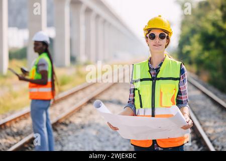 Ritrattista donne in cantiere su binari ferroviari con project manager di lavoro su rotolo di progetto in linea di trasporto periferico Foto Stock