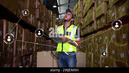 Immagine di una rete di connessioni con icone su un lavoratore maschio caucasico che prende appunti in magazzino Foto Stock