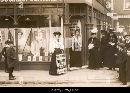 Negozio Kensington Women's Social & Political Union, Mary Sinclair in piedi all'esterno del negozio con il poster "Vittoria attraverso la prigione" insieme a bambini e altre suffragette, volantini, bandiere e un'immagine di Emmeline Pankhurst in vetrina, iscrizione a matita sul retro "Mary Sinclair, Kensington, 1910" Foto Stock