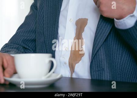 Irriconoscibile un uomo con un vestito ha versato caffè su una camicia bianca nel caffè. Macchie di caffè marrone sporche sui vestiti. concetto di colorazione della vita quotidiana. Foto Stock