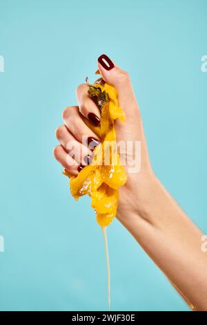 giovane modella sconosciuta con smalto per unghie che stringe succoso cachi in mano su sfondo blu Foto Stock