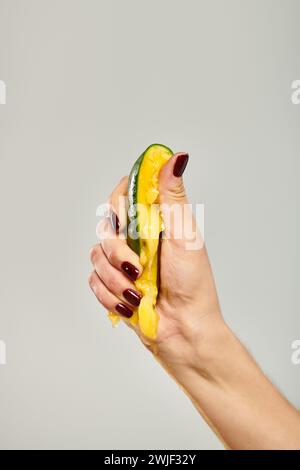 giovane modella sconosciuta con smalto per unghie che stringe mango fresco in mano su sfondo grigio Foto Stock