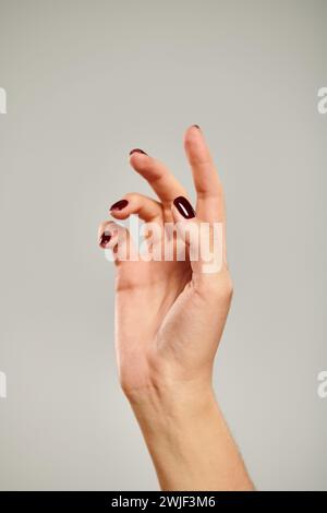 mano con smalto scuro di giovane modella femminile sconosciuta che punta verso l'alto su sfondo grigio Foto Stock