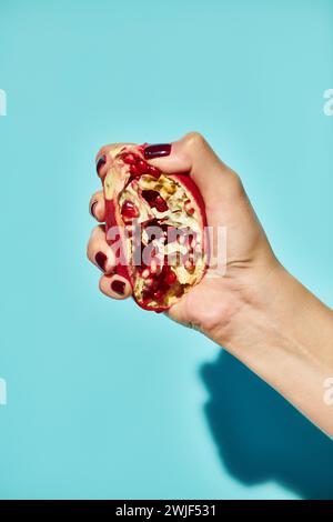 modella femminile sconosciuta che spreme delizioso melograno su sfondo blu vivace, foto dell'oggetto Foto Stock