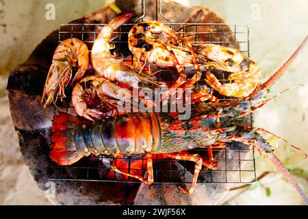 Grigliate di pesce sulla spiaggia. Aragosta, gamberi e barbecue di pesce. Pranzo salutare durante le vacanze estive al mare. Crostacei, calamari e gamberi grigliati sul fuoco. Foto Stock