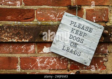 Cartello con la scritta Please keep dogs on lead, nella campagna del Regno Unito, appeso su un muro di mattoni rossi, West Horsley, Surrey, Inghilterra, Regno Unito, 2024 Foto Stock