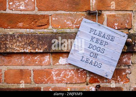 Cartello con la scritta Please keep dogs on lead, nella campagna del Regno Unito, West Horsley Place, appeso su un muro di mattoni rossi Foto Stock