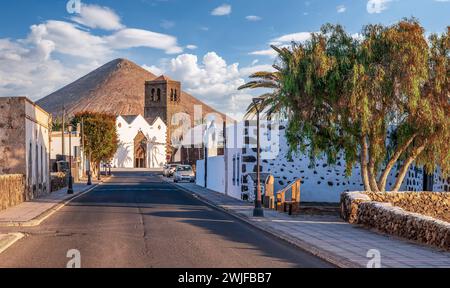 Scoprite la bellezza serena della Chiesa la Candelaria a la oliva, Fuerteventura, annidata sotto una maestosa montagna in uno storico villaggio delle Canarie. Foto Stock