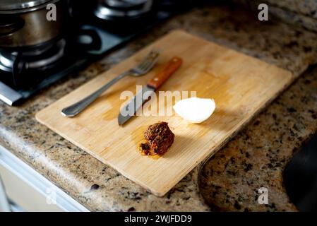 Tagliere in legno con lama, forchetta, carne e cipolla sulla parte superiore. Preparazione del pranzo. Foto Stock