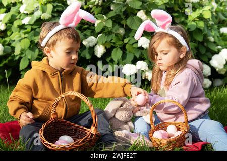 Bimbo e bambina con orecchie da coniglio con cesti con uova durante la tradizionale festa di Pasqua in un giorno di sole Foto Stock