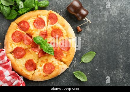 Pizza al peperoni. Tradizionale pizza al peperoni e ingredienti da cucina pomodori e basilico su un vecchio tavolo di fondo in cemento. Cucina tradizionale italiana Foto Stock