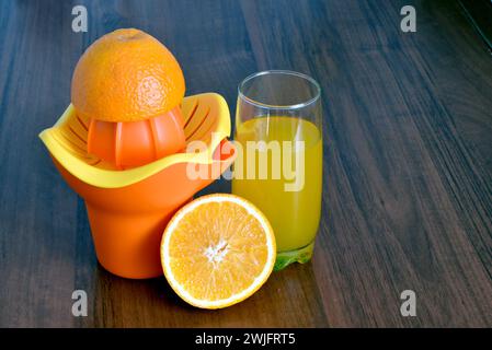 Mangiare sano. Sul tavolo della cucina c'è un bicchiere di succo di frutta fresco, un'arancia e una centrifuga. Foto Stock