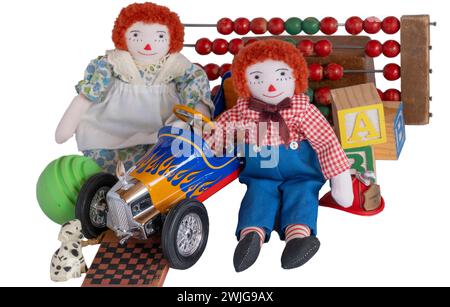 Raggedy Ann & Andy, vecchie bambole di stracci fatte a mano, siediti circondati da giocattoli d'epoca; blocchi di legno, palla, auto da corsa, cane, dama, cappello, contatore perline. Foto Stock