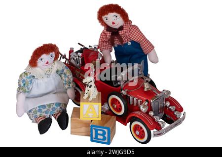 Bambole di stracci fatte a mano, Raggedy Ann & Andy collocate tra giocattoli, blocchi, motore antincendio, cane piccolo, cappello da pompiere, vecchi e nuovi giocattoli in legno e metallo. Isolato Foto Stock
