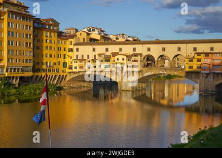 La luce del sole mattutino sul Ponte Vecchio, sul Ponte Vecchio, Firenze, Italia, con bandiera UE in primo piano Foto Stock