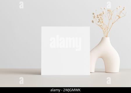 Mockup con carta d'invito quadrata con decorazione gypsophila sul tavolo beige. Foto Stock